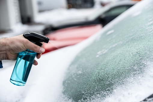 Spraying de-icer on a frosted windshield on a snowy day in Edmonton & Leduc, AB